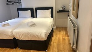 Une chambre double avec deux lits, un radiateur, une étagère avec des articles de toilette et un porte-serviettes fixé au mur.