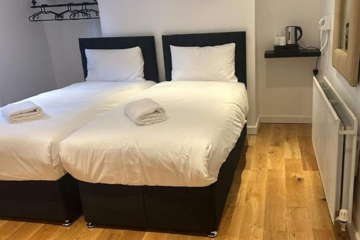 A double room with two beds, a radiator, a shelf with toiletries, and a wall-mounted towel rack.