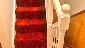 Un escalier dont les marches sont recouvertes d’une moquette rouge et dont les balustres sont blanches.