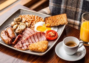 A breakfast tray with eggs, bacon, sausages, mushrooms, beans, toast, and a glass of orange juice.