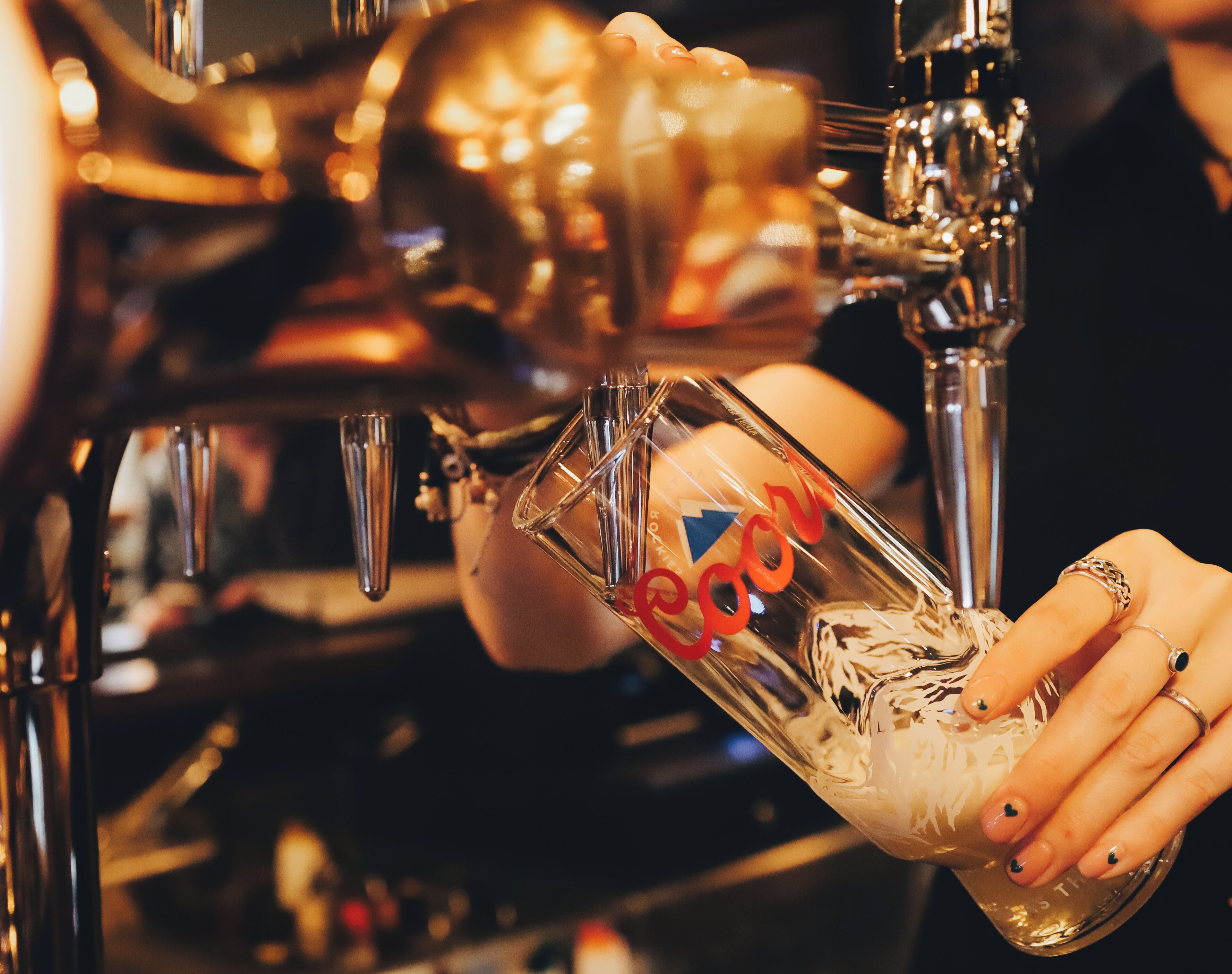 Une personne verse une boisson d’un robinet dans un verre transparent orné d’un motif en forme de cœur.