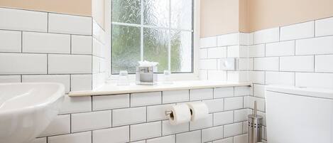 A bathroom with white tiles, a window, a sink, and a toilet.