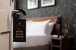 A hotel room with a bed, a nightstand, and a sign on the door that reads "The Inn Collection please do not disturb."