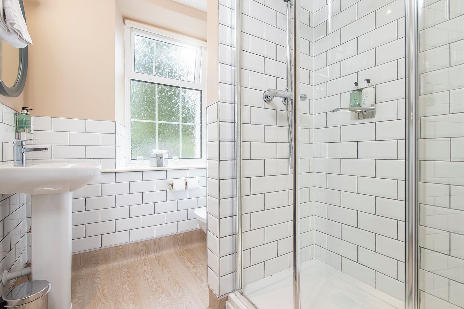 A modern bathroom with white subway tiles, a glass shower enclosure, a sink, and a window with frosted glass.