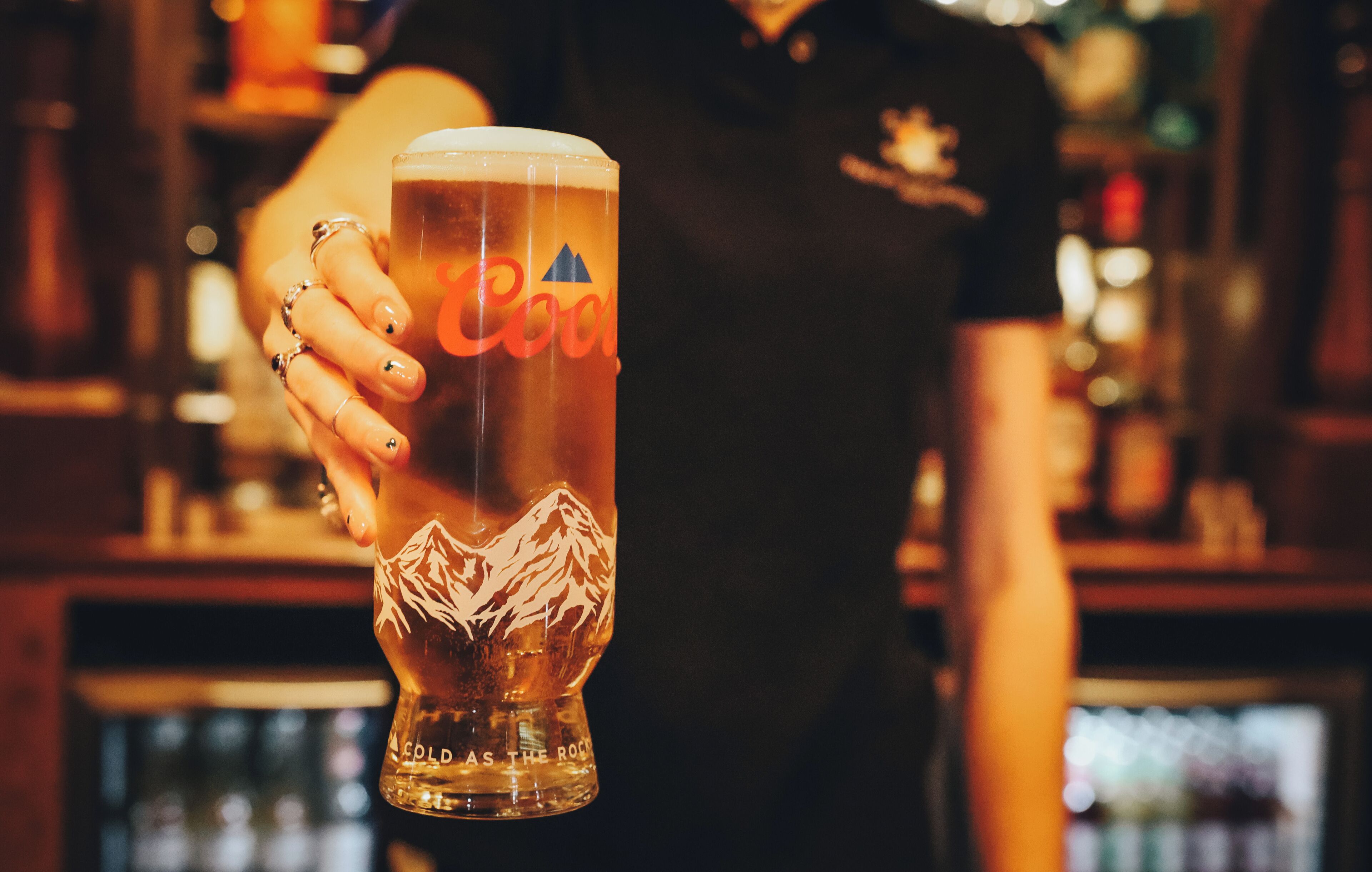 A person holding a glass with a mountain design and the text "Cold as the Rock" on it.