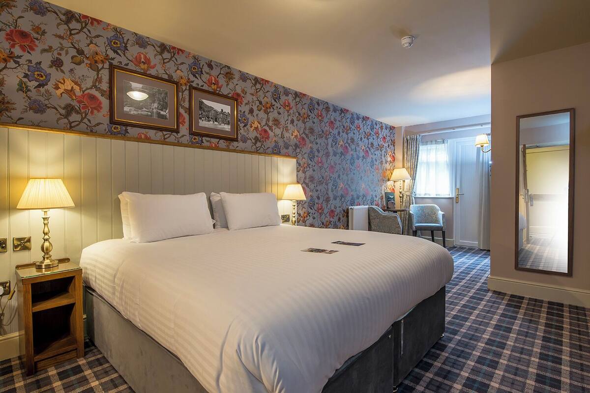 A hotel room with a large bed, two bedside lamps, a floral wallpaper, and a checkered floor.