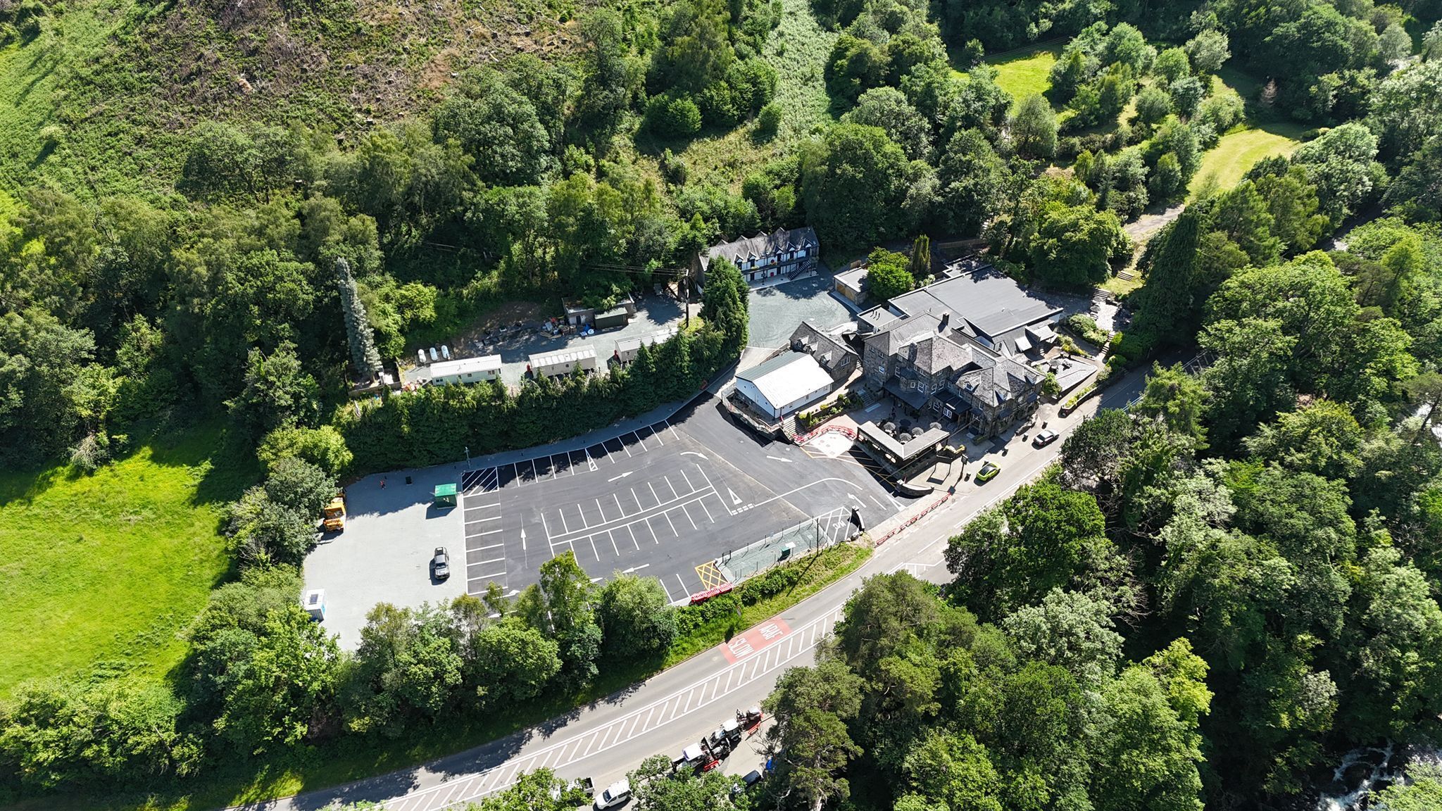 An aerial view of a hotel with a parking lot, surrounded by dense greenery.