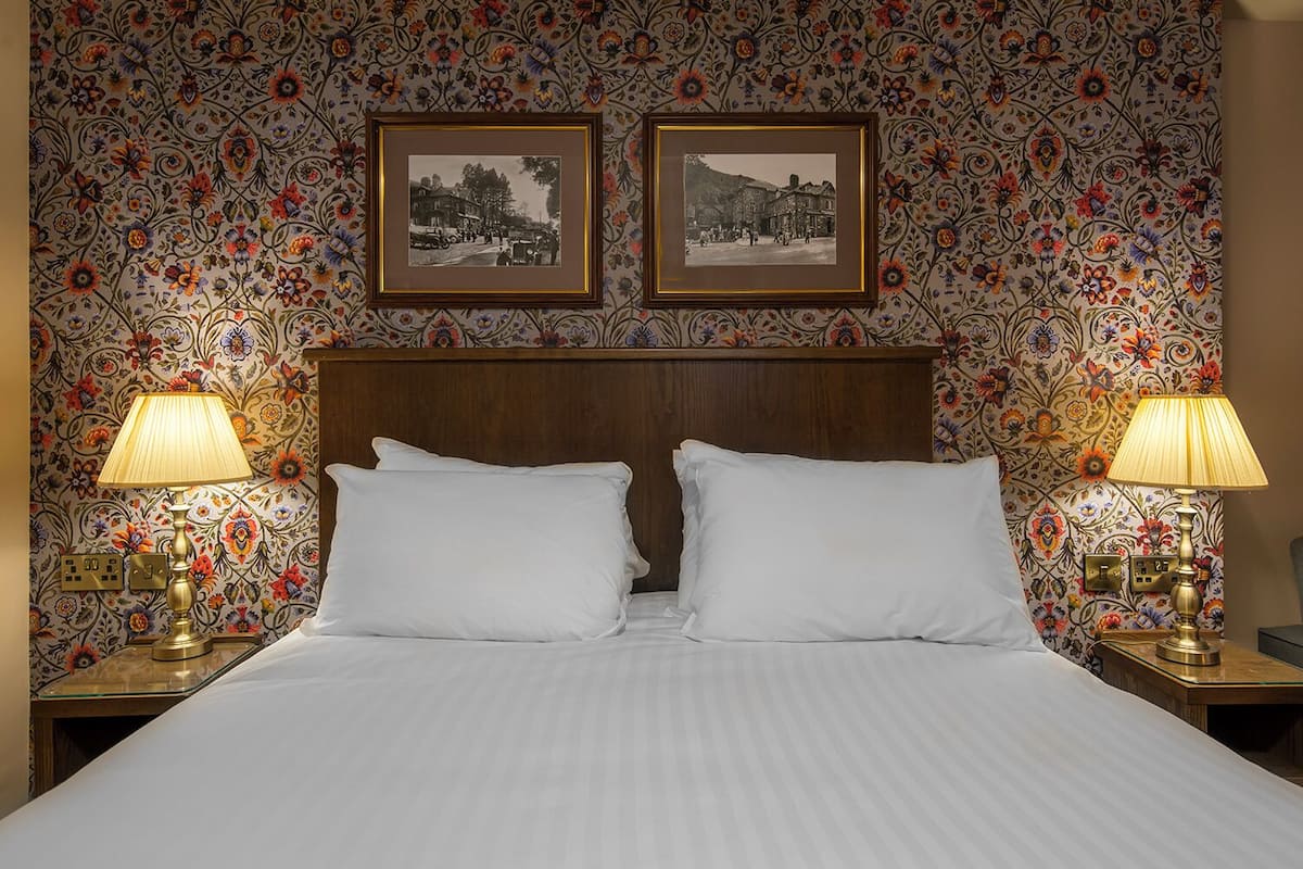 A hotel room with a bed, two nightstands, two lamps, and two framed pictures on the wall.