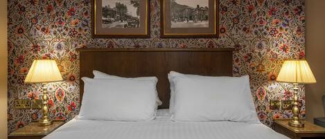 A hotel room with a bed, two nightstands, two lamps, and two framed pictures on the wall.