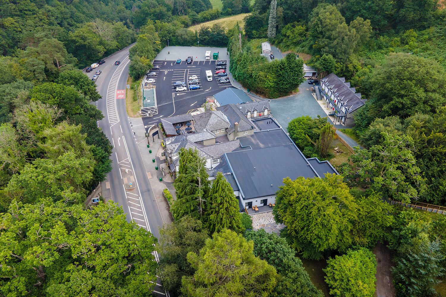 Et luftfoto viser en bygning med parkeringsplads, omgivet af frodig vegetation.