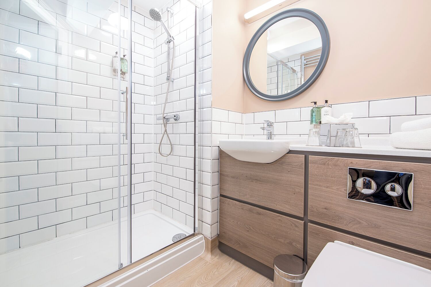 Un baño moderno con cabina de ducha de vidrio, tocador de madera y espejo redondo.
