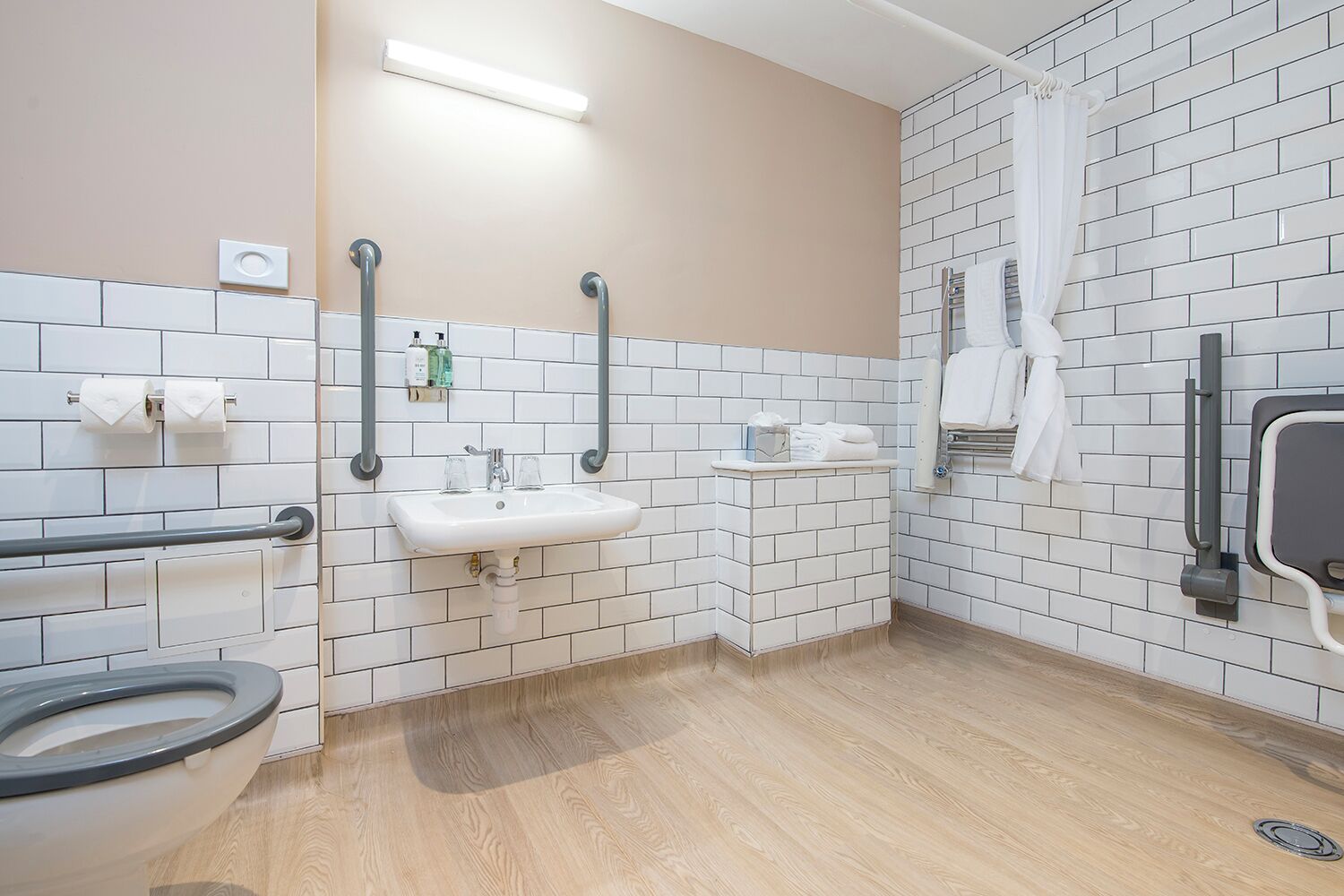 A modern bathroom with a toilet, sink, and shower area, equipped with grab bars and a hand dryer.