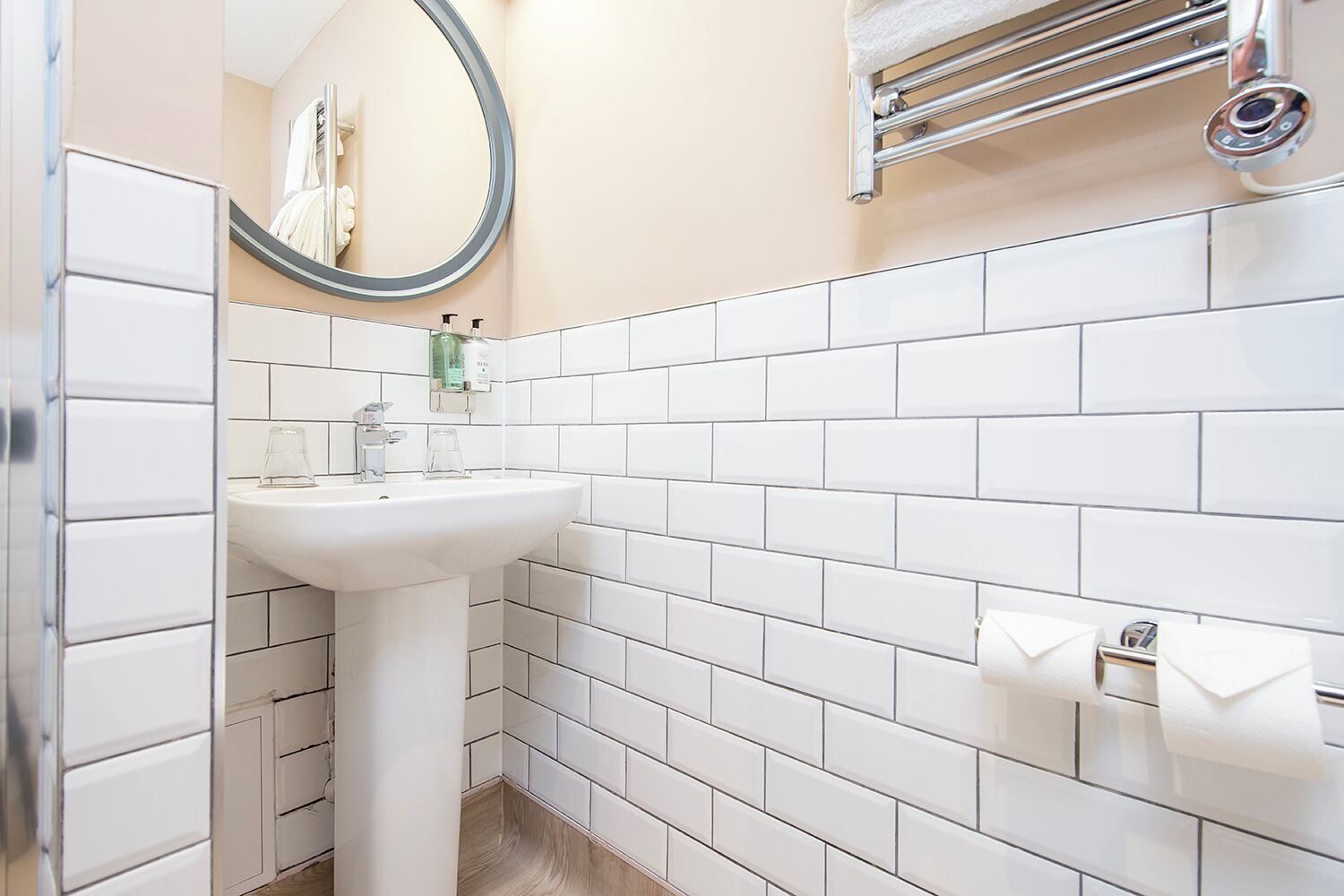 A bathroom with white tiles, a sink, a mirror, and a towel rack.