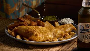 A plate of fish and chips with a bottle of beer and a hand squeezing a lemon.