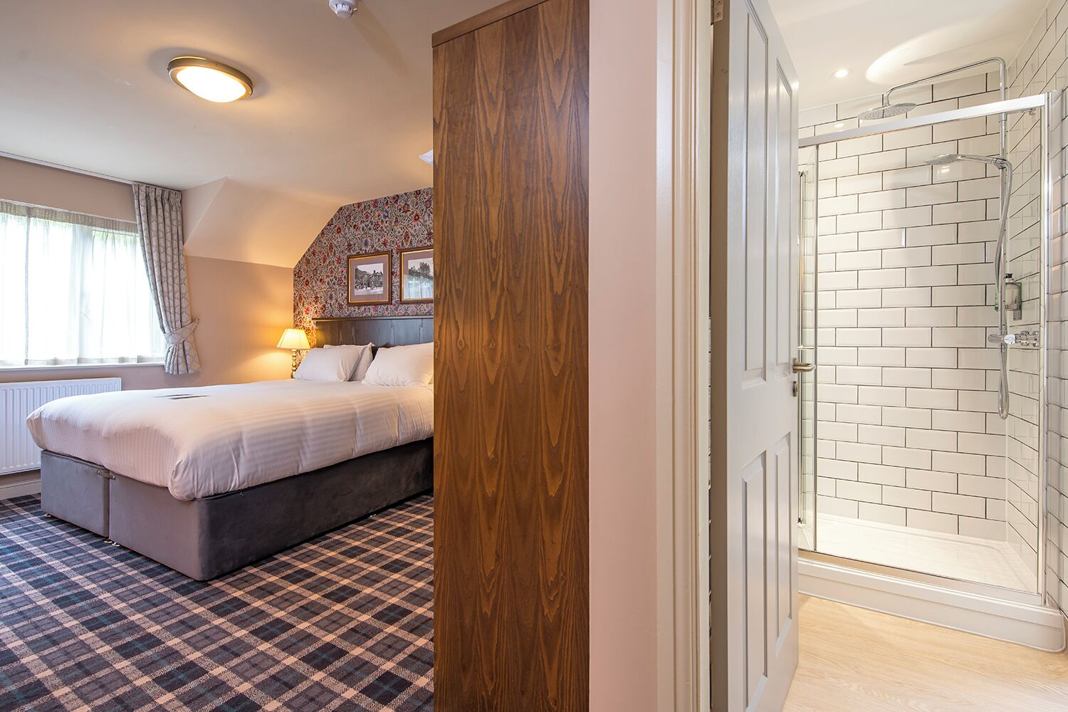Ein Schlafzimmer mit Bett, Nachttisch, Lampe, Fenster mit Vorhängen, einer Wand mit Muster und einer Duschkabine mit Fliesen.