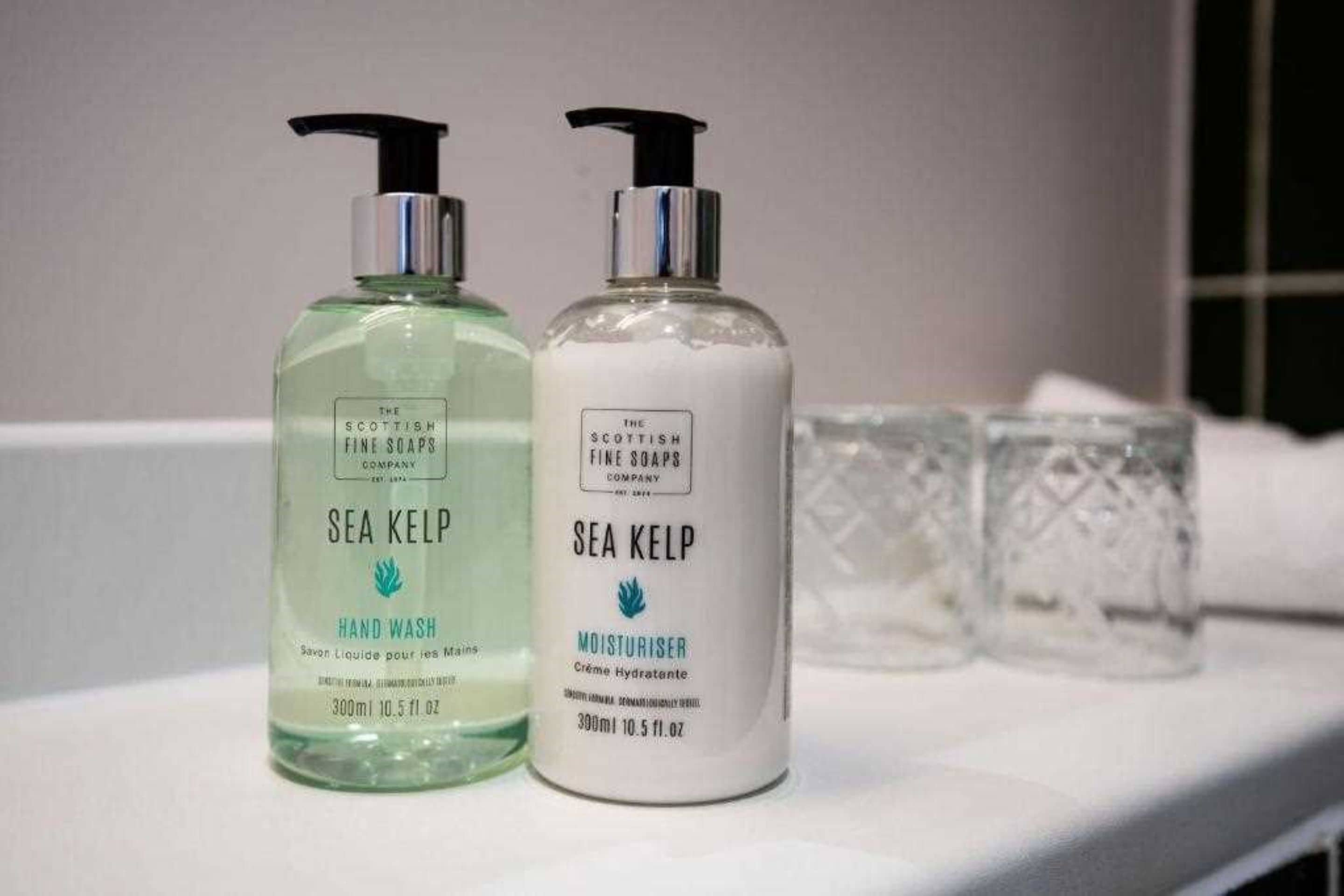 Två flaskor med handtvål och handkräm från The Scottish Fine Soaps Company, båda med doft av tång, placerade på en vit yta tillsammans med två genomskinliga glas.