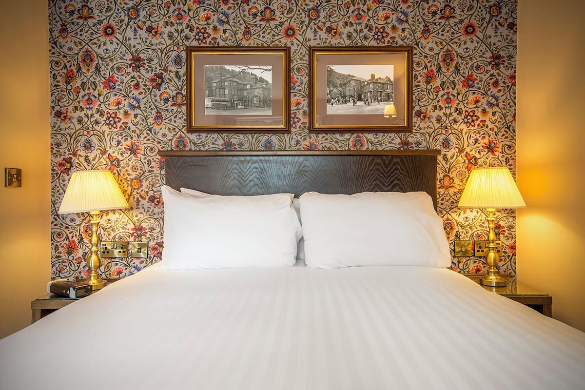 A hotel room with a large bed, two bedside lamps, and floral wallpaper.
