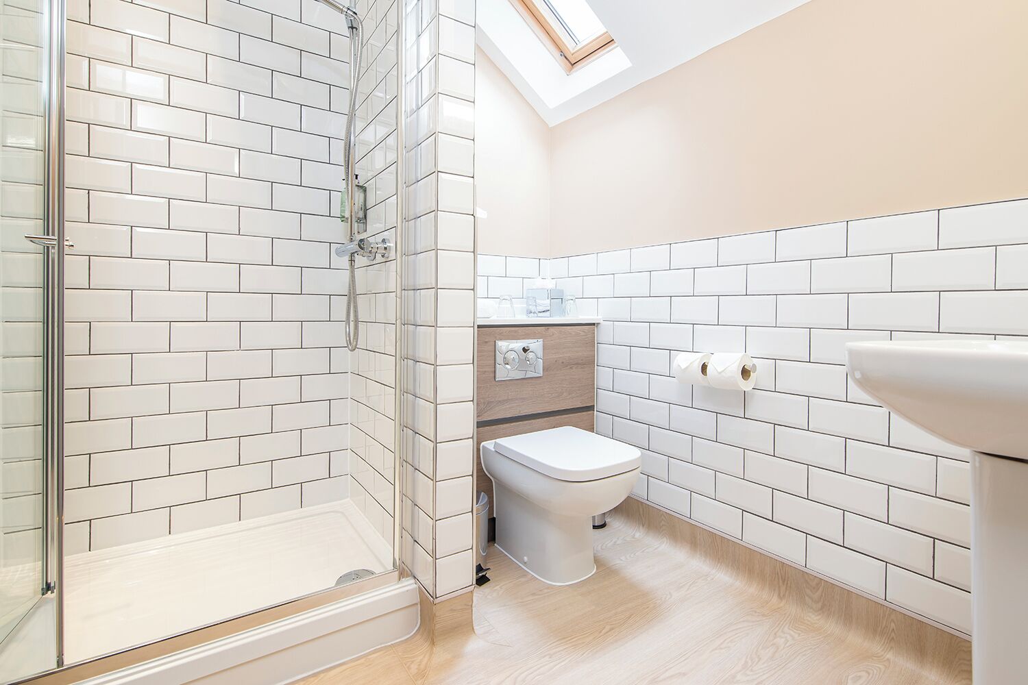 Un baño con paredes de azulejos blancos, cabina de ducha con mampara de vidrio, inodoro y lavabo.
