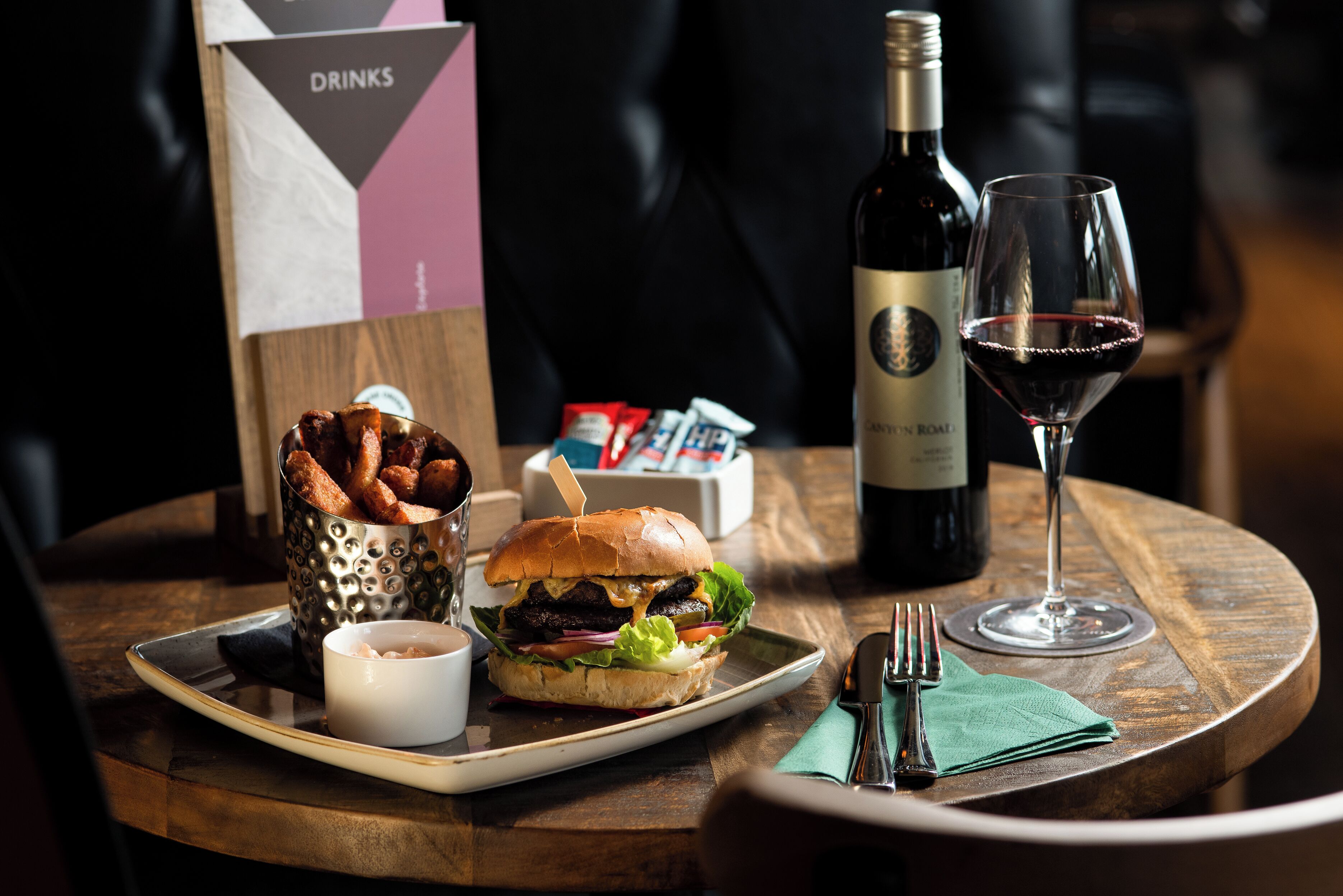 Un plateau repas avec un hamburger, des frites et une boisson, posé sur une table en bois.