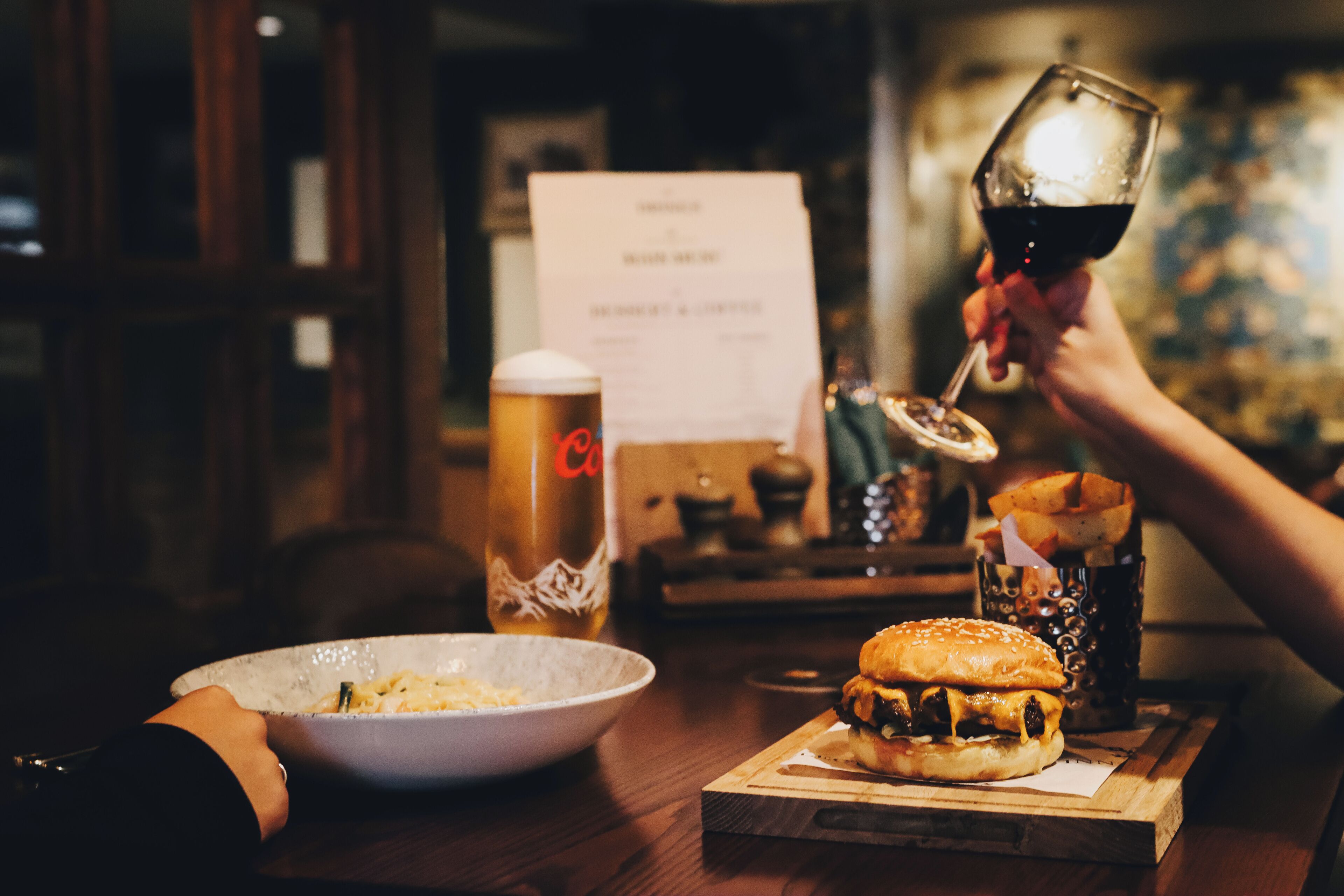 Ein Esstisch mit einem Hamburger, einem Glas Rotwein, einem Bierkrug und einer Speisekarte.