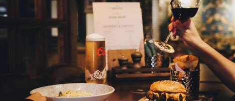 A dining table with a burger, a glass of red wine, a beer mug, and a menu.