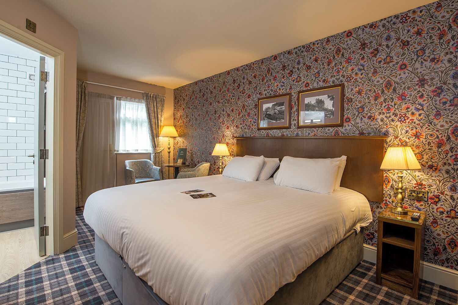 A hotel room with a large bed, two bedside tables with lamps, a chair, a small table, and a door leading to a balcony.