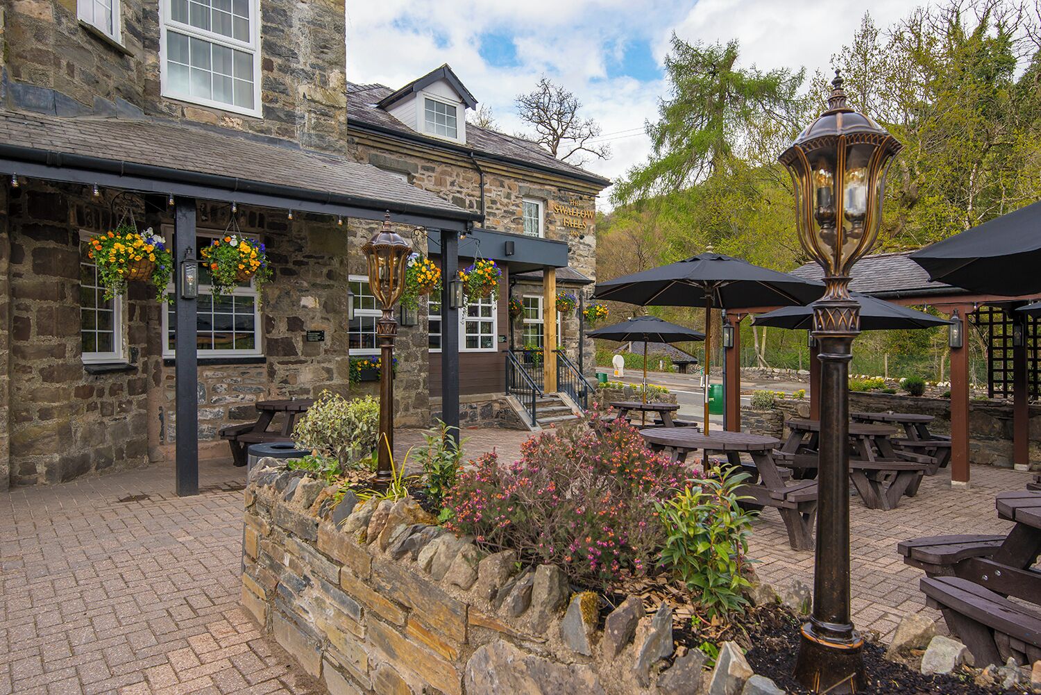 A stone building with outdoor seating and hanging flower baskets.