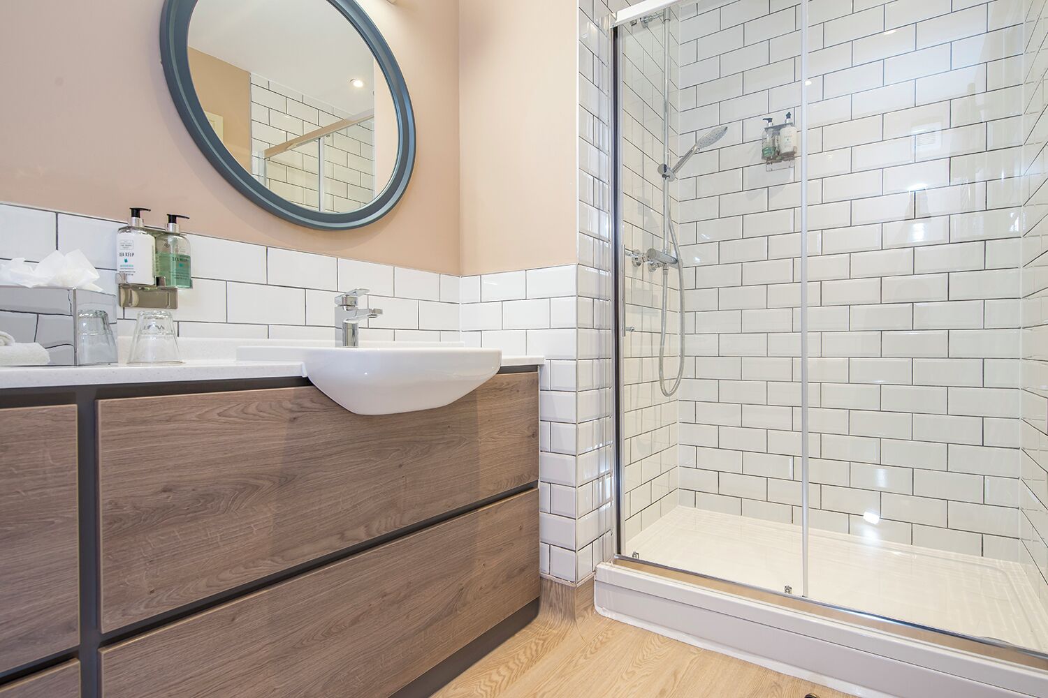 A modern bathroom with a white sink, wooden vanity, and a glass shower enclosure.