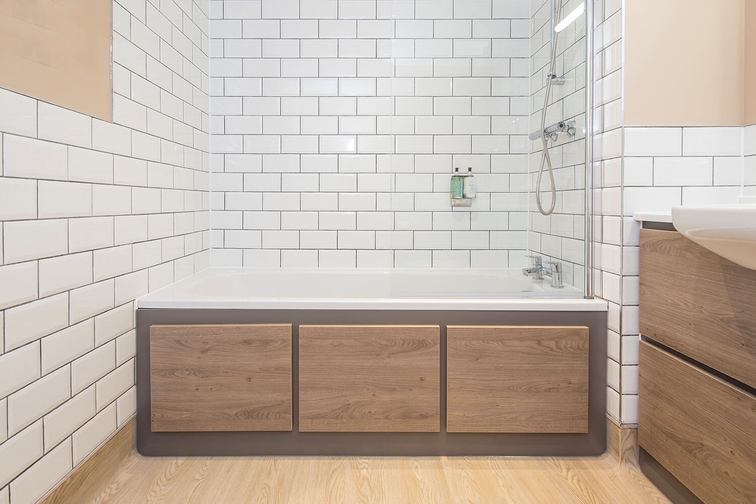 A modern bathroom with white subway tiles, a wooden cabinet, a bathtub, and a shower area.
