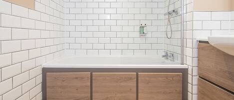 A modern bathroom with white subway tiles, a wooden cabinet, a bathtub, and a shower area.