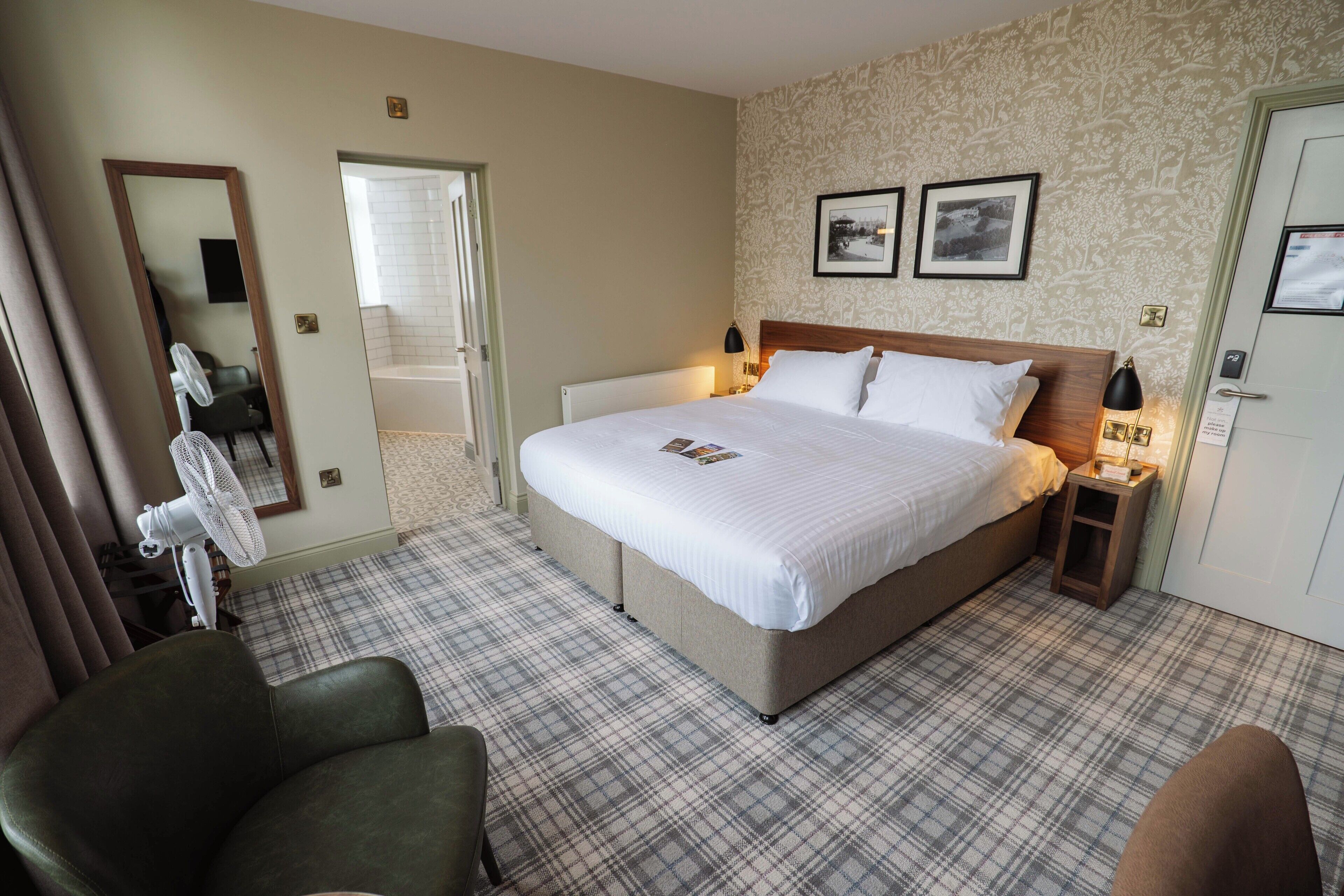 A hotel room with a large bed, two bedside tables, a chair, a mirror, and a door.