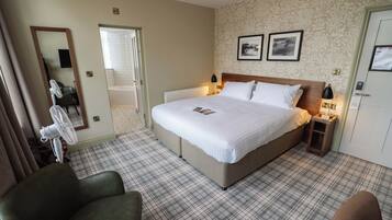 Una habitación de hotel con una cama grande, dos mesitas de noche, una silla, un espejo y una puerta.