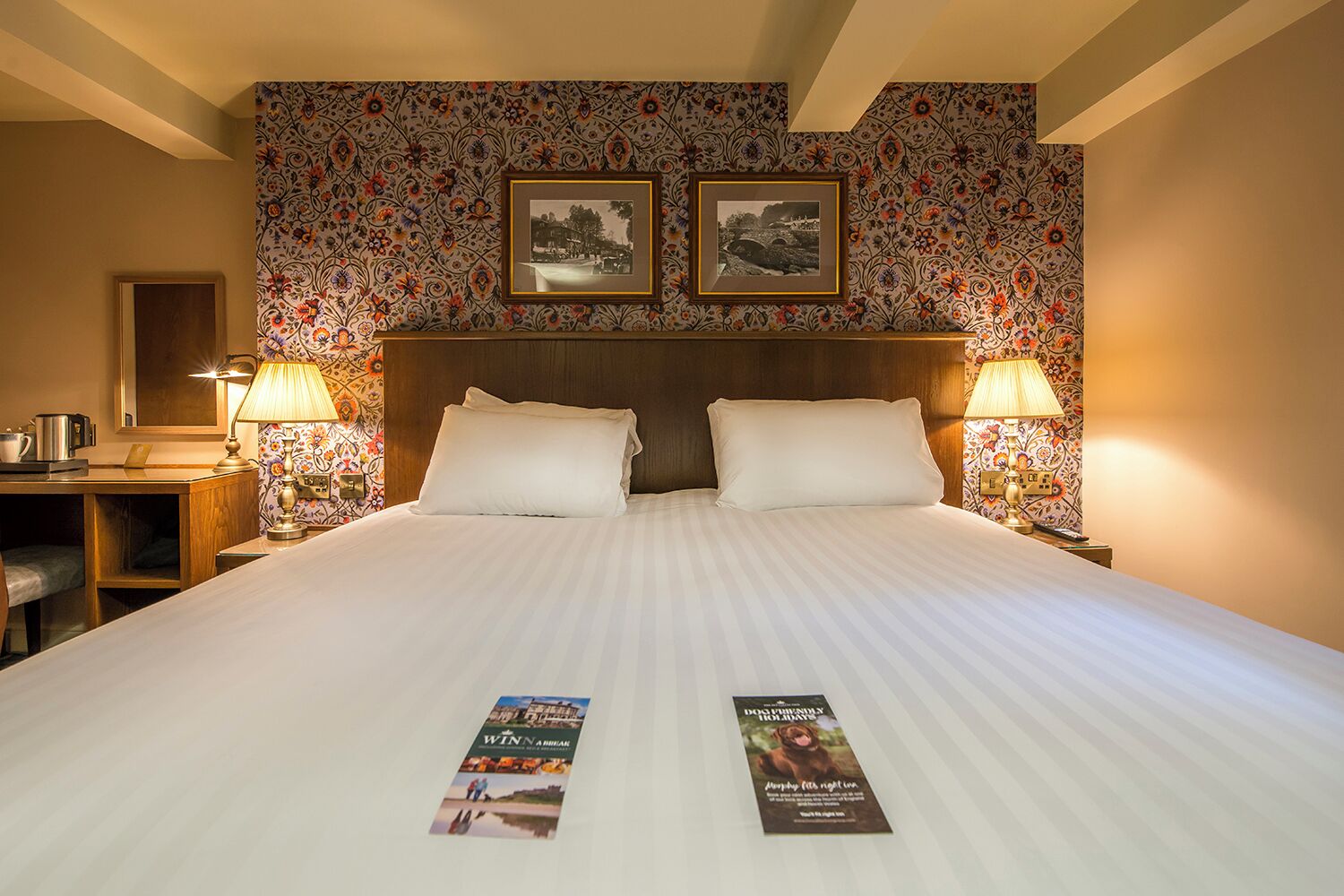 Habitación de hotel con una cama grande, dos mesitas de noche con lámparas, un escritorio con silla y dos cuadros en la pared.