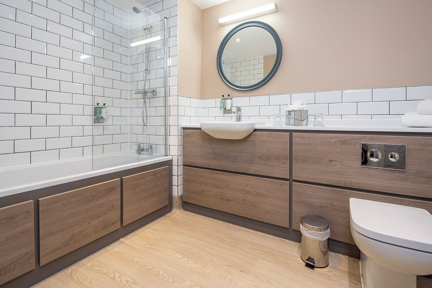 Et moderne badeværelse med en glasbrusekabine, en trævaskebord, håndvask med spejl og toilet.