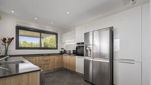 A modern kitchen with stainless steel appliances, wooden cabinets, and a large window. - Villa Kimloa - Three Bedroom Villa, Sleeps 6 (Case-Pilote)