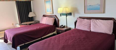 Habitación de hotel con dos camas, un escritorio, una silla, una lámpara y dos cuadros en la pared.