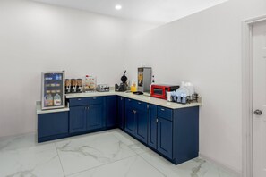 A compact kitchen with dark blue cabinets, a white countertop, a coffee machine, a microwave, and a refrigerator.