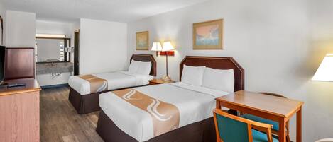 A hotel room with two beds, a desk, a chair, a lamp, and a painting on the wall.