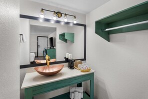 A bathroom with a copper sink, a mirror with lights, and a green vanity.