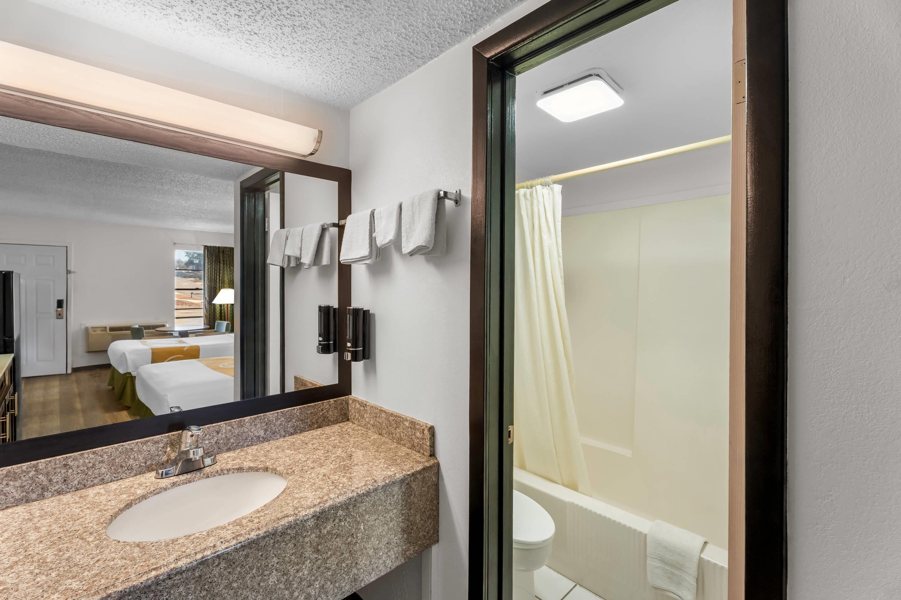 Un baño moderno con un lavabo de granito, un espejo grande, un inodoro y una ducha con cortina.