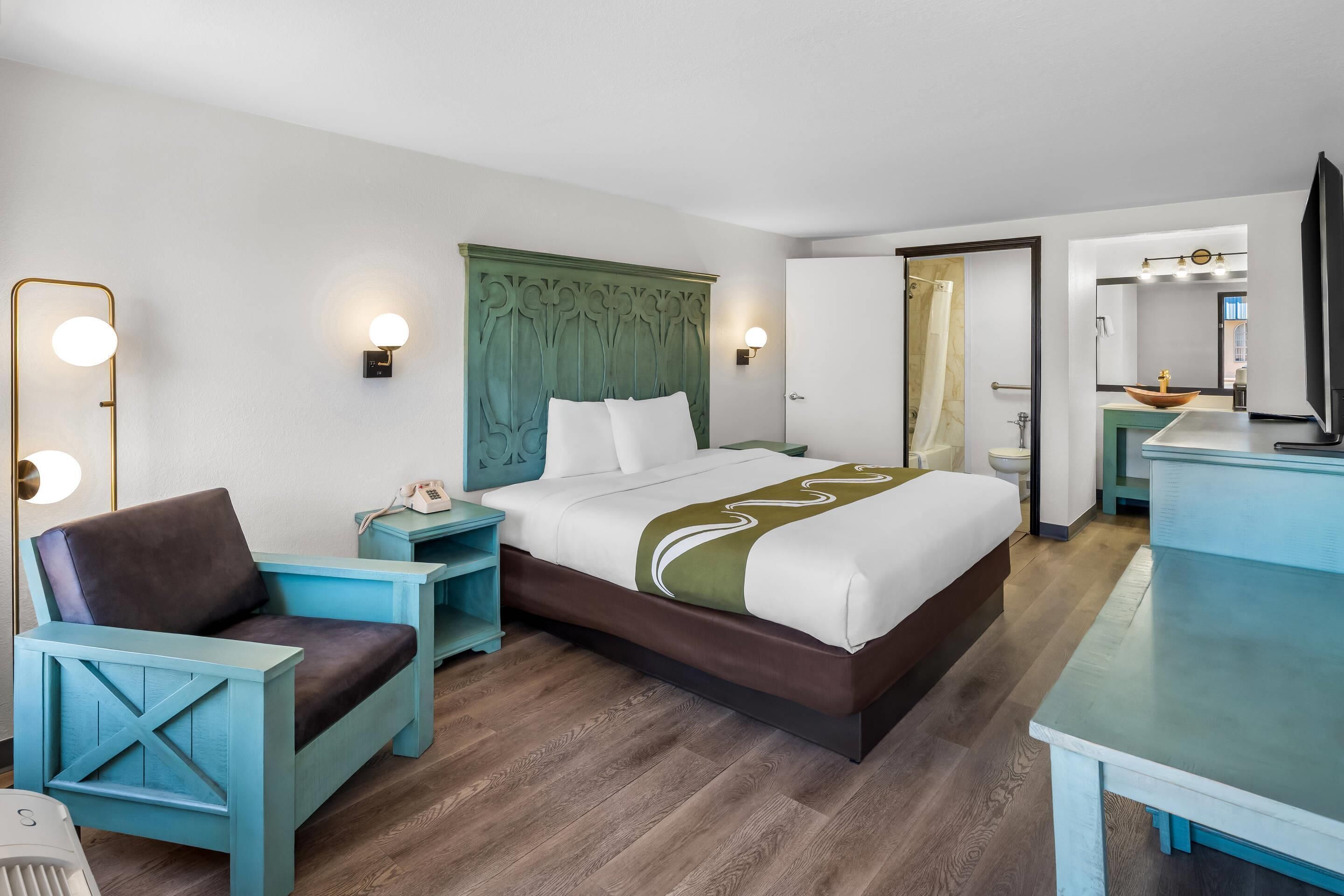 A modern hotel room with a bed, a chair, a desk, and a television.