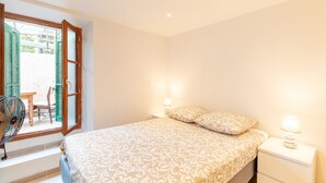 Un dormitorio con una cama, dos lámparas de noche, un ventanal con contraventanas verdes y un ventilador.