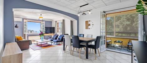 A modern living room with a dining area, large windows, and a view of the outdoors.