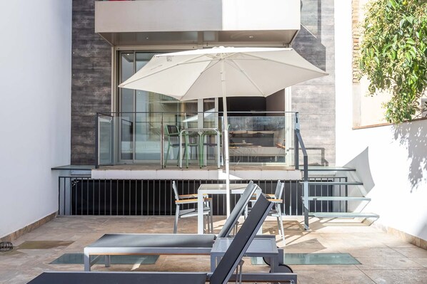 A modern outdoor seating area with a glass balustrade, a white umbrella, and a staircase leading to an upper level.