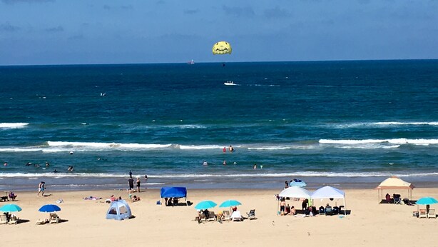 Una playa con sombrillas, toldos y gente.