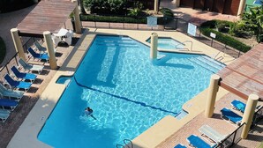 Una piscina con trampolín, sillas de descanso y una zona vallada.