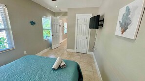 A bedroom with a bed, a TV mounted on the wall, and a door leading to another room. - Turtle Nest Beach House (Fort Myers Beach)