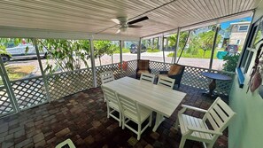 A covered patio area with a table and chairs, a ceiling fan, and a view of the street. - Turtle Nest Beach House (Fort Myers Beach)