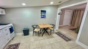 Een eetgedeelte met een tafel, stoelen, een prullenbak en een schilderij aan de muur.