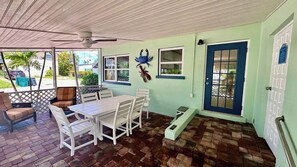 A covered patio area with a table and chairs, a ceiling fan, and a door with a window. - Turtle Nest Beach Studio (Fort Myers Beach)